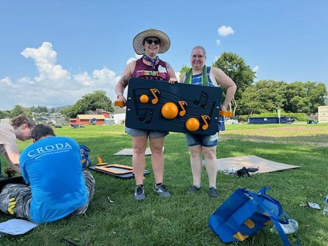 Two UGI employees hold a piece of the playground they assembled which features bright orange musical notes.