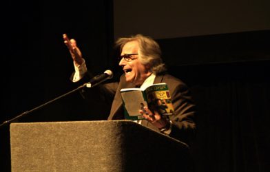 Henry Winkler standing at podium reading his book.